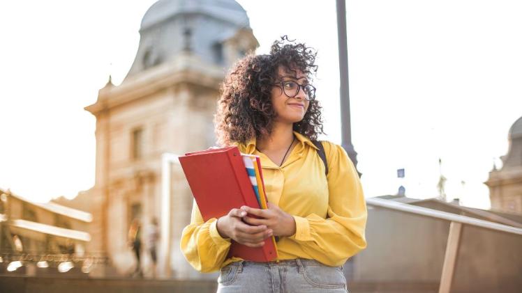 a student standing in front of a city landmark holding a folder